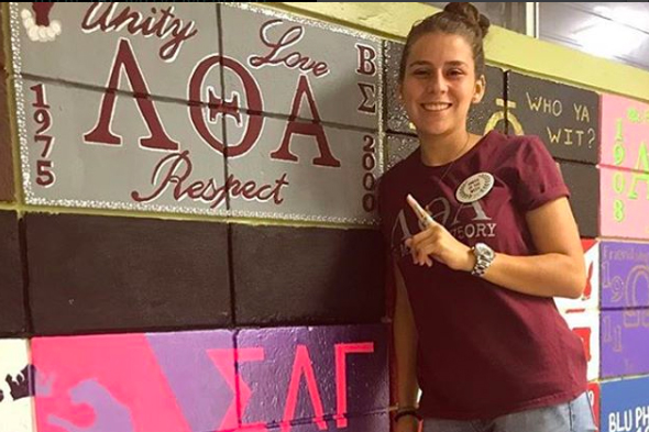 Student poses next to Lambda Theta Alpha wall sign